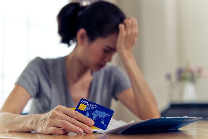 Stressed young sitting Asian woman hands holding credit card and