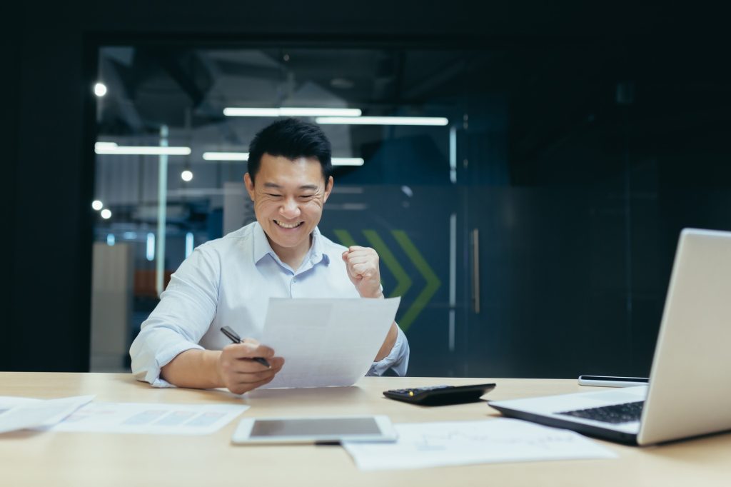 An Asian accountant sitting in the office with documents. He is happy with the loan, the budget