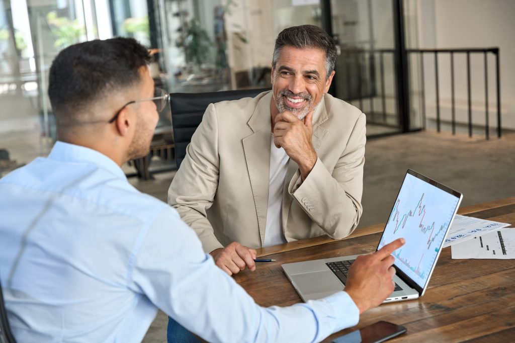 Financial advisor consulting stock market investor showing charts on laptop.